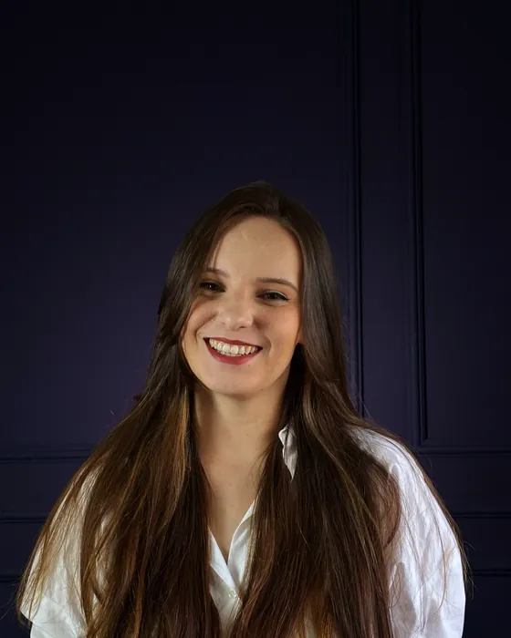 Luana Fontana Petri sorrindo, de camisa branca, em fundo azul-escuro