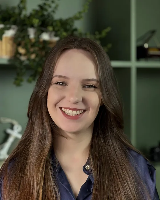 Luana Fontana Petri sorrindo, de blusa azul-marinho, em frente à estante