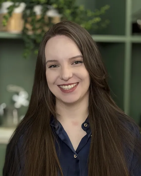 Luana Fontana Petri sorrindo, de blusa azul-marinho, ao lado da estante